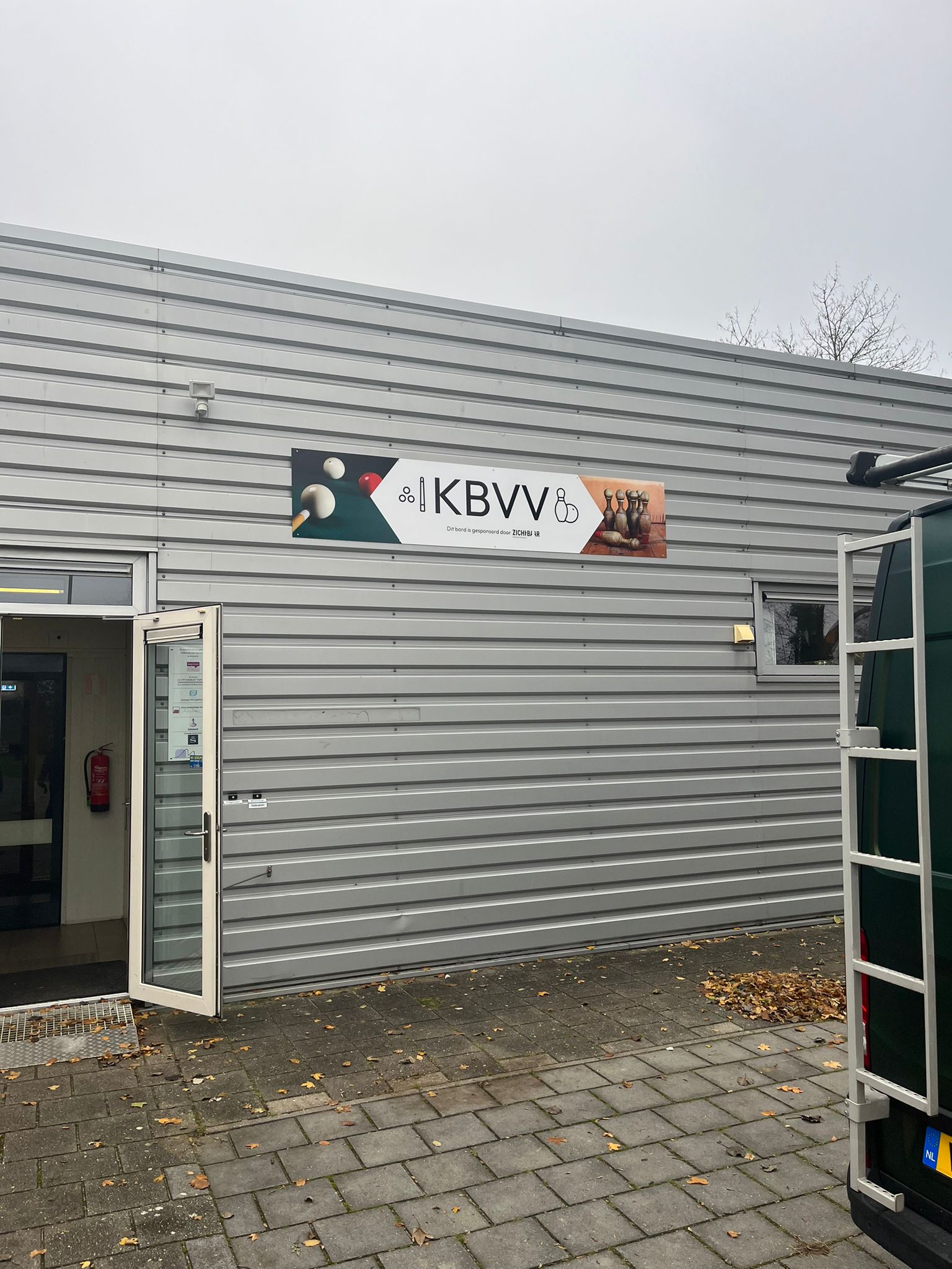 Reclamebord aan de gevel bij de ingang van kbvv